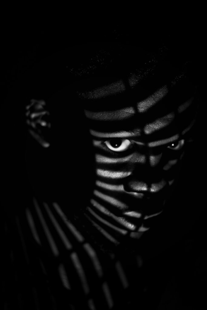 Moody black and white portrait of a man with dramatic shadow patterns on the face.